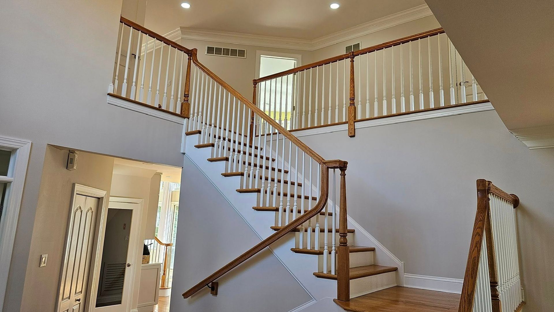 Grand staircase with white balusters, wood handrails, and a light-colored wall.