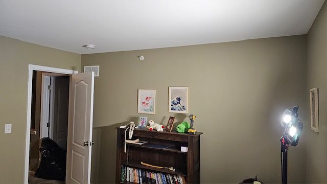Room interior with olive green walls, bookshelf, and open doorway. Two framed pictures hang above the bookshelf.