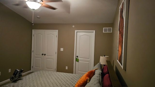 Bedroom with a bed, two white doors, and a ceiling fan. Brown walls and a large framed artwork are present.