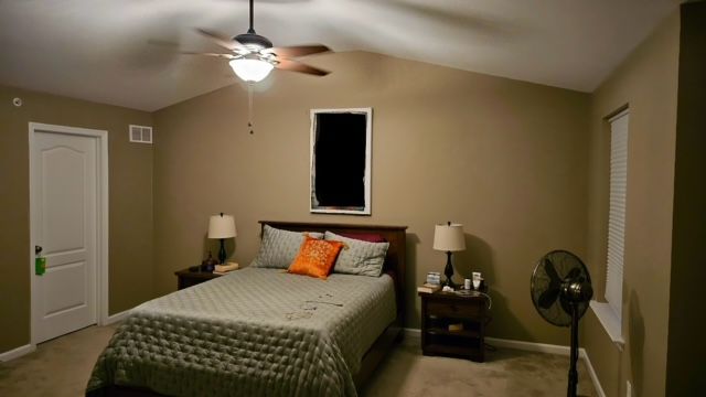 Bedroom with bed, nightstands, fan, door, and window. Tan walls, ceiling fan, and a comforter on the bed.