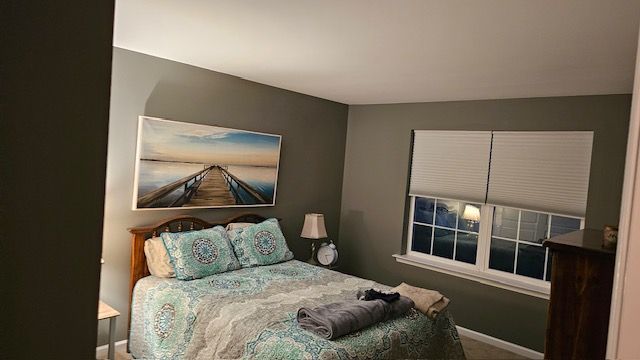 Bedroom with a bed, artwork, and window. Green-gray walls, a wooden bed frame, and soft lighting.