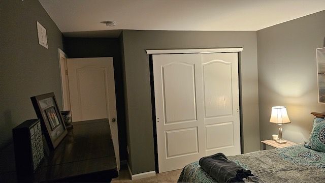 Bedroom with a white closet, gray walls, a dresser, and a bed with a lamp.