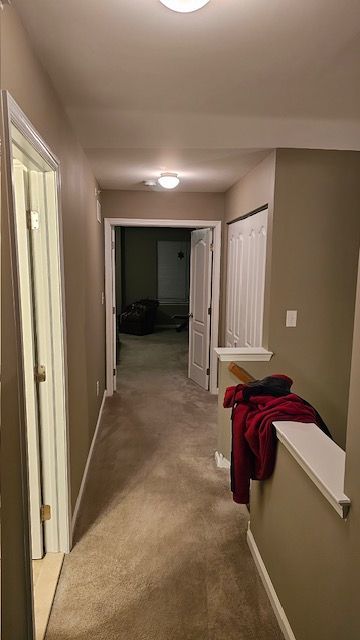 Hallway with beige walls, carpet, and doorways. A blanket and clothes sit on a railing.