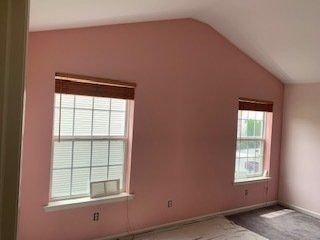 Pink-walled room with two windows, bamboo shades, and a vaulted ceiling.