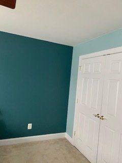 Room interior with teal accent wall, light blue wall, white closet doors, and beige carpet.