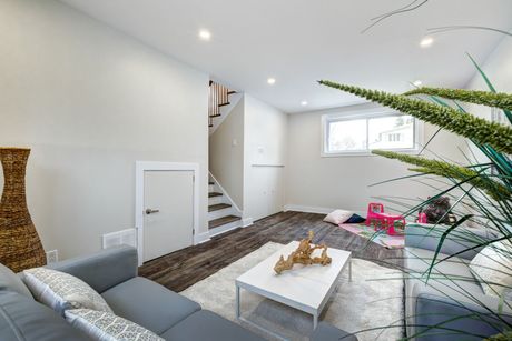 Living room with gray sofa, white rug, and wood-look flooring. Stairs lead to the upper level.