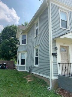 Two-story light blue house with white trim, green lawn, and trees.