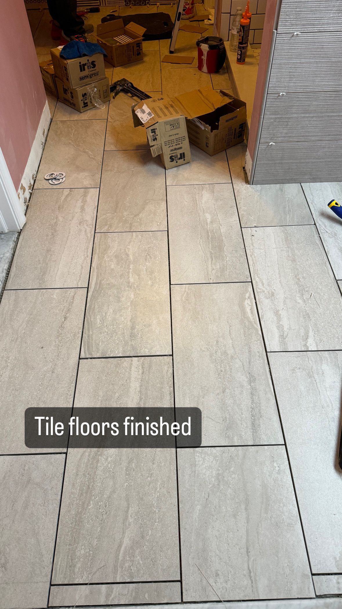 Finished tile floor installation in a hallway. Beige rectangular tiles, with boxes and supplies visible in background.