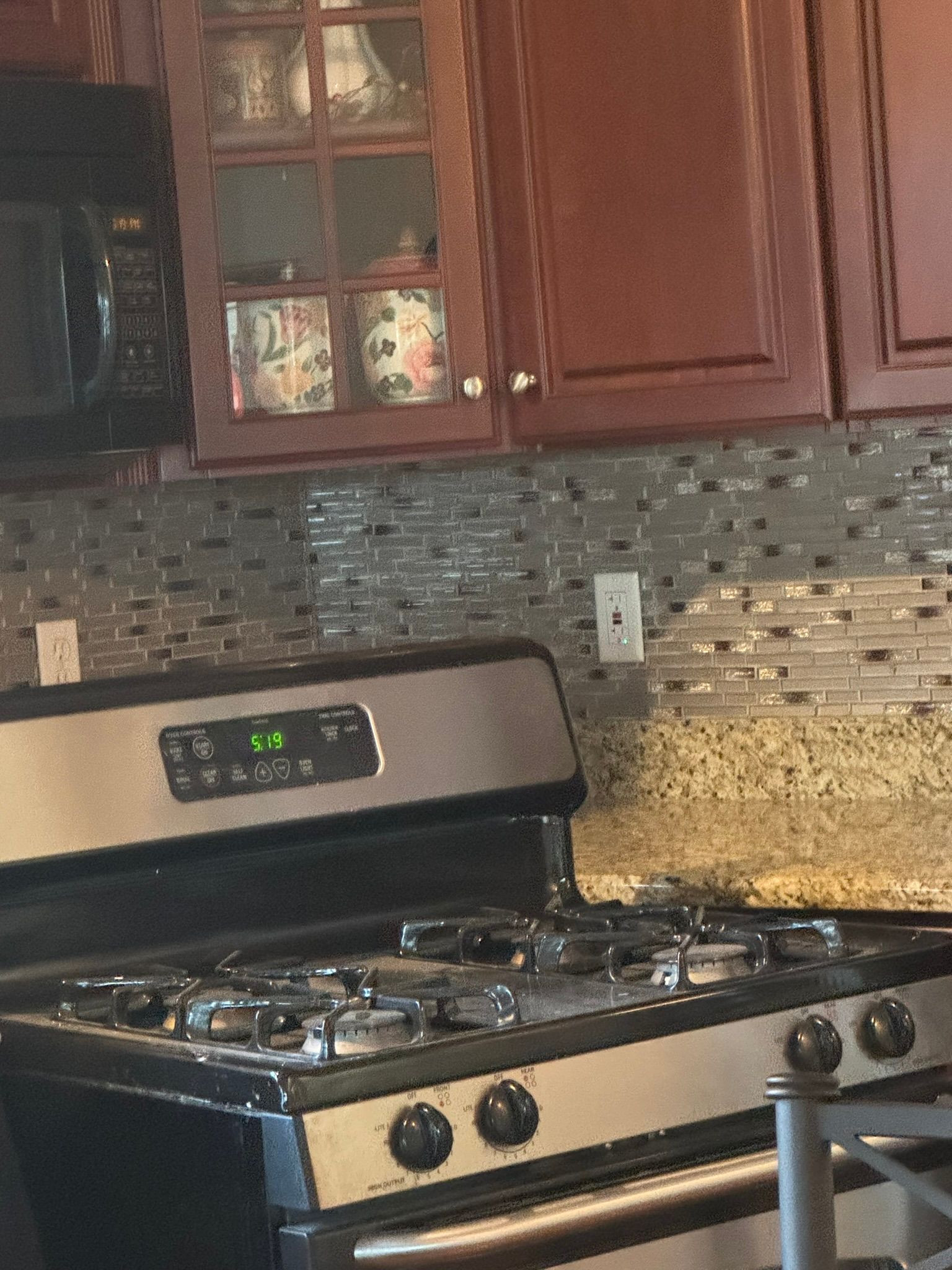 Stainless steel gas stove in a kitchen with brown cabinets and tiled backsplash.