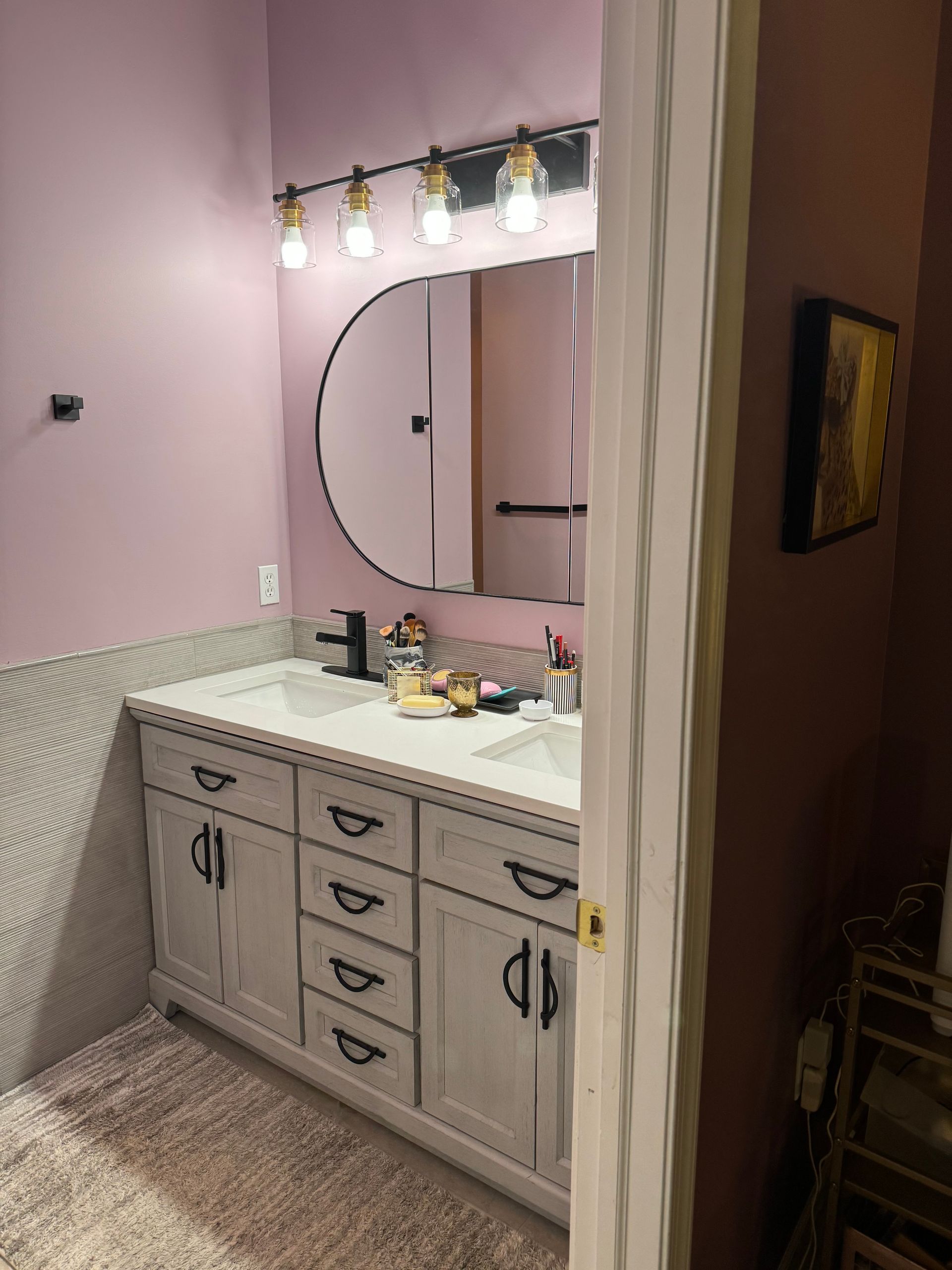 Bathroom with pink walls, white vanity, round mirror, and overhead light.