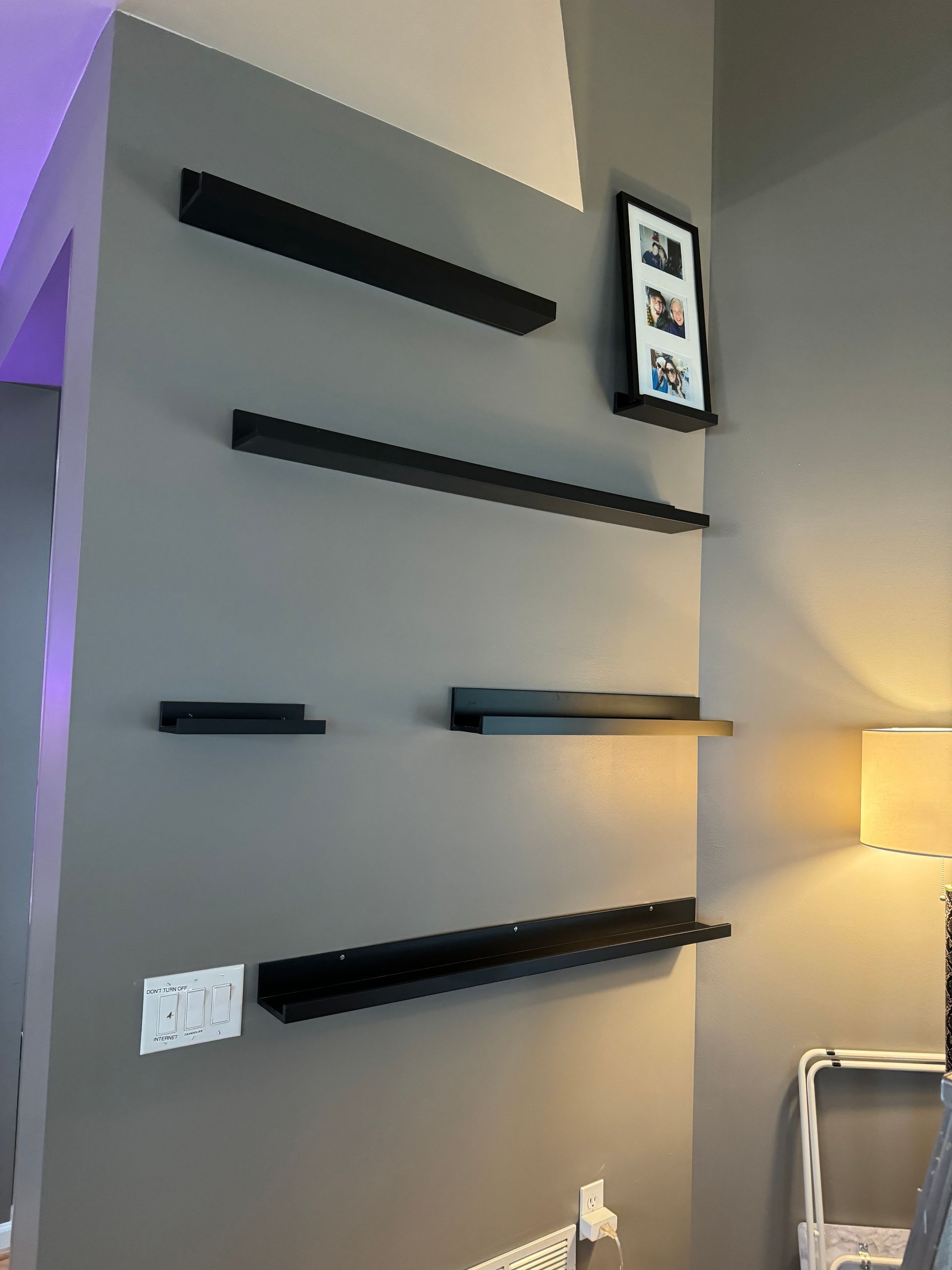 Gray wall with four black shelves and a picture frame. A light fixture is to the right.