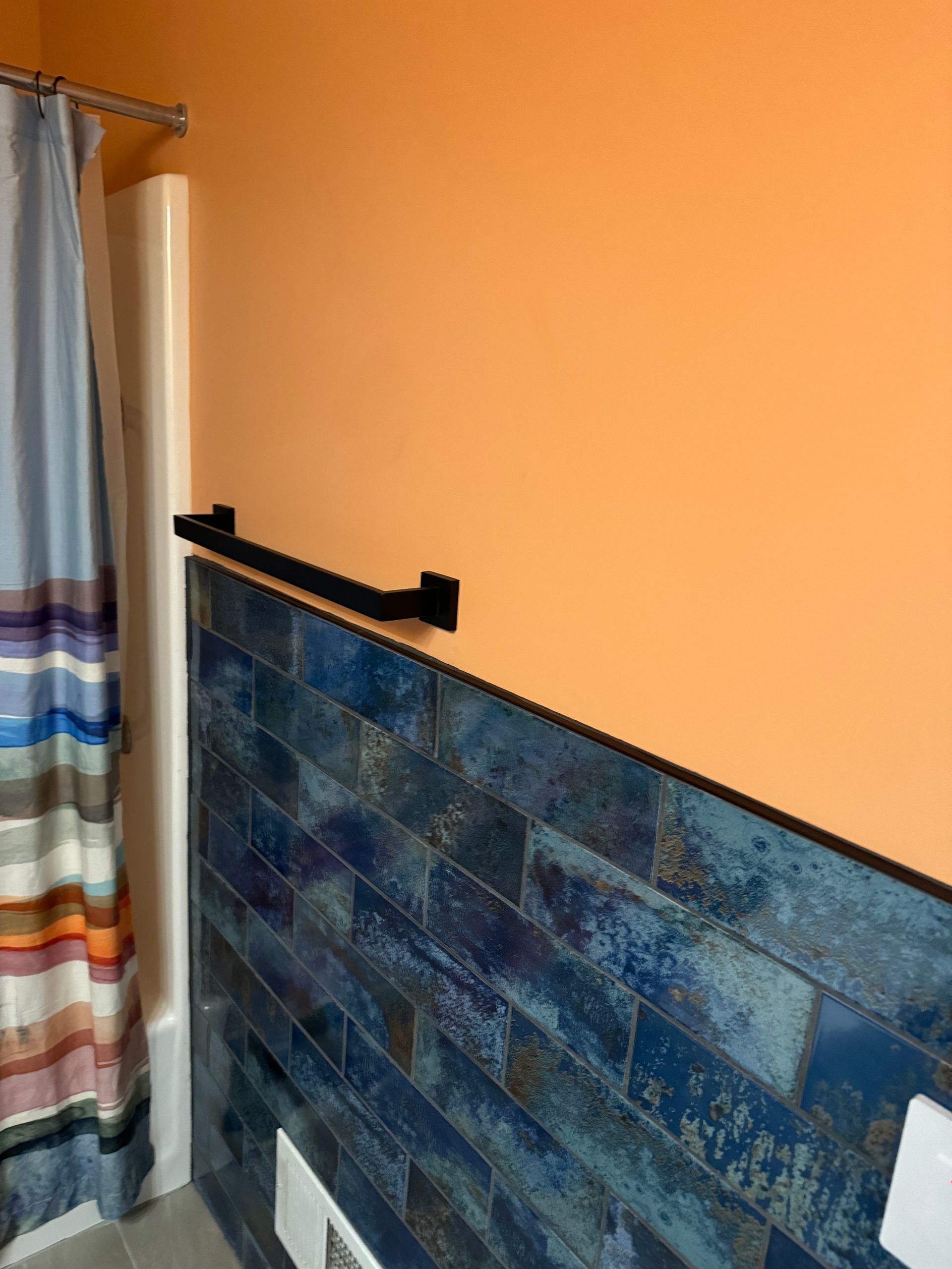 Bathroom with blue tiled wall, orange wall, black towel bar, and striped shower curtain.