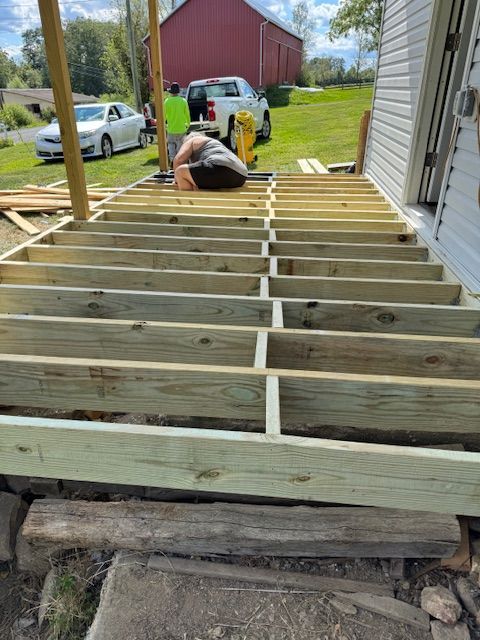 A person working on a deck frame. The frame is made of wood, and the setting is outdoors.