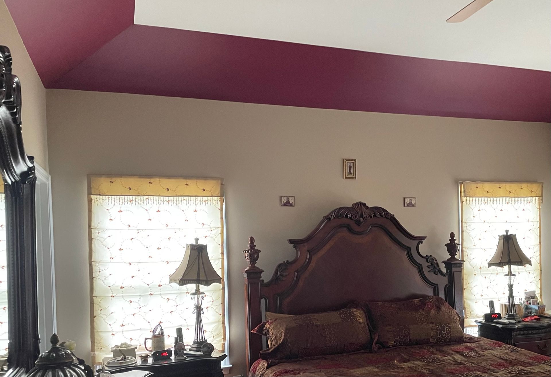 Bedroom with a burgundy ceiling, two windows with blinds, a large bed with a dark headboard, and two lamps.
