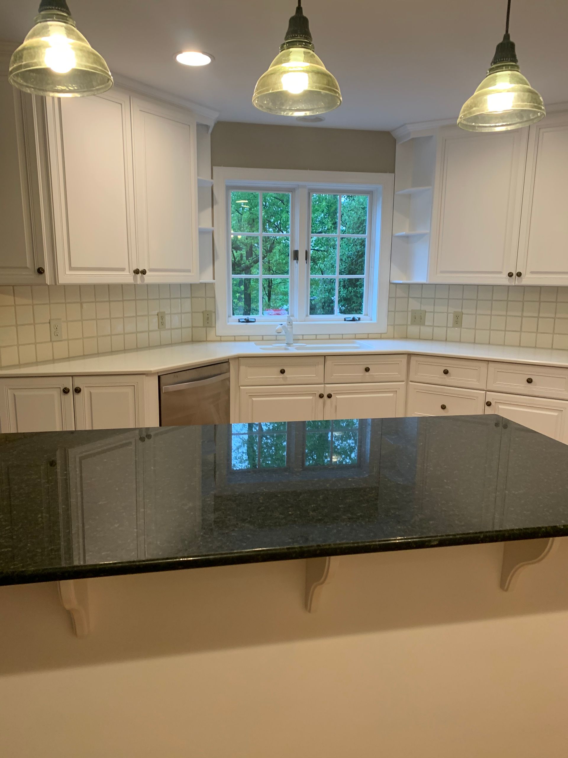 White kitchen with dark granite countertop island; hanging lights over the island; window with view.