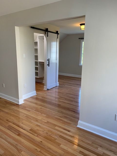 Hardwood-floored room with a barn-style door opening to a closet. A bedroom is visible in the background.