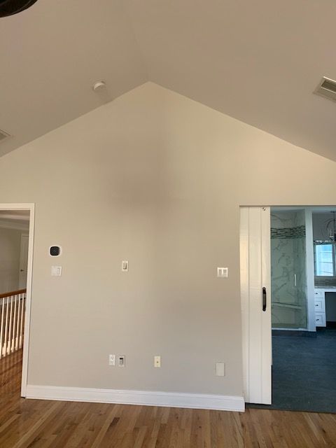 Interior room with tall, angled ceiling, light gray walls, wooden floor, and a sliding door.