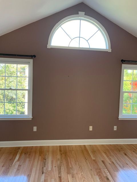 Interior room with brown walls, wood floor, arched and rectangular windows.