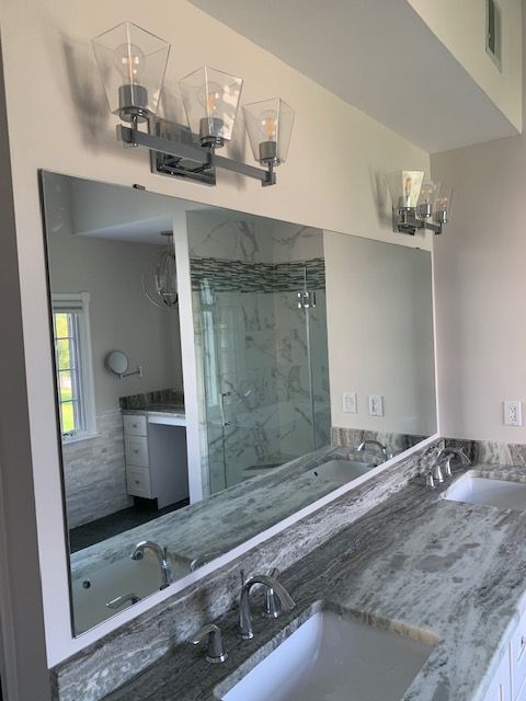 Bathroom with a large rectangular mirror over a double vanity, with overhead light fixtures.