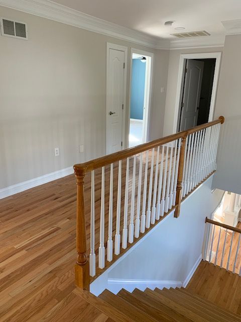 Hallway with wooden floor and staircase. White banister, tan railing, light gray walls, and white trim.