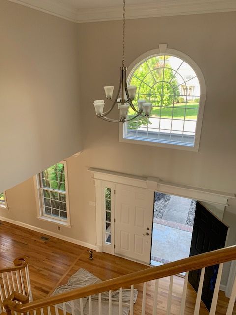 High-angle shot of a home entryway with a chandelier, two windows, and wooden staircase.