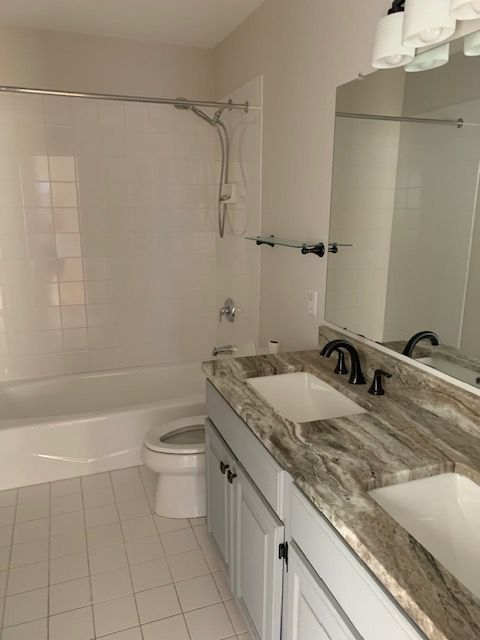 Bathroom with white tile, a bathtub, toilet, double sink vanity, and a large mirror.