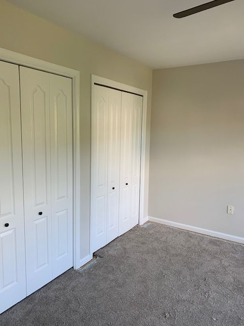 Empty bedroom with two white closet doors, beige walls, and gray carpet.