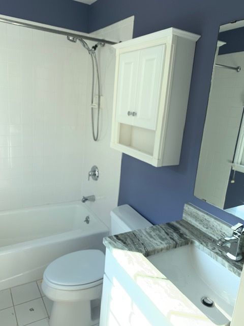 Bathroom with white tub, toilet, and cabinet against blue wall; granite countertop.