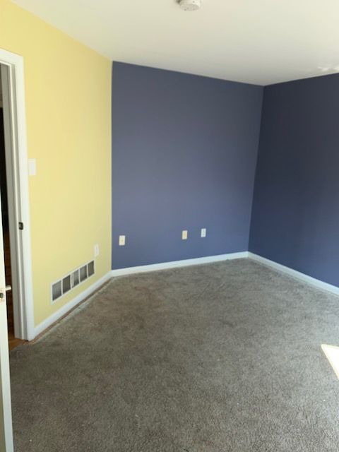 Empty room with yellow and blue walls, white trim, and gray carpet.