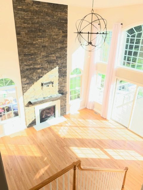 Interior view: Living room with stone fireplace, hardwood floors, large windows, and an orb chandelier.