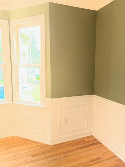 Room interior with white trim, green walls, wooden floor, and a window.