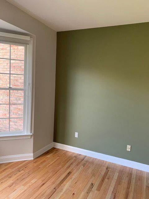 Empty room with hardwood floors, a bay window, and walls painted green and beige.