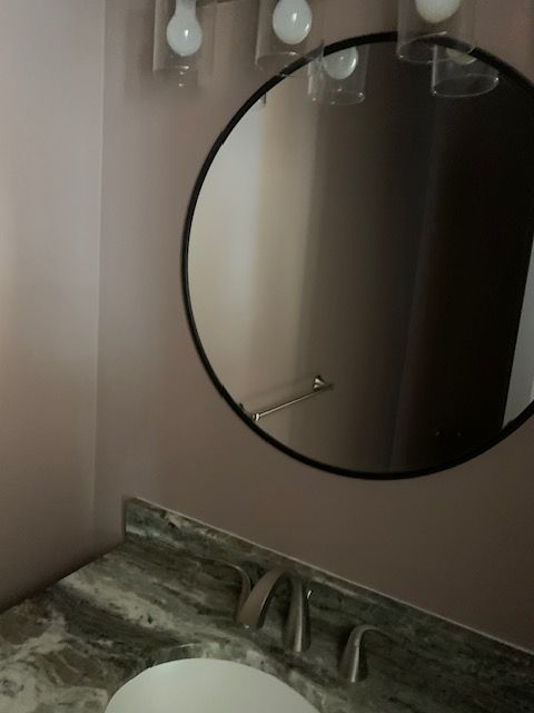 Bathroom with round mirror, gray countertop, white sink, and light bulbs above the mirror.