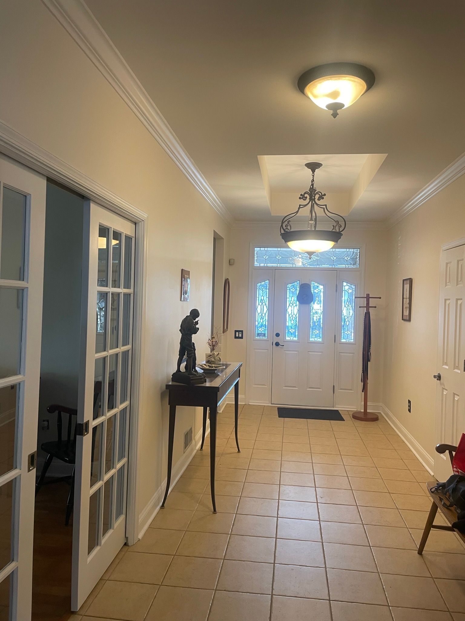 Hallway with tile floor, glass doors, and ornate lighting fixtures. A table holds a sculpture.