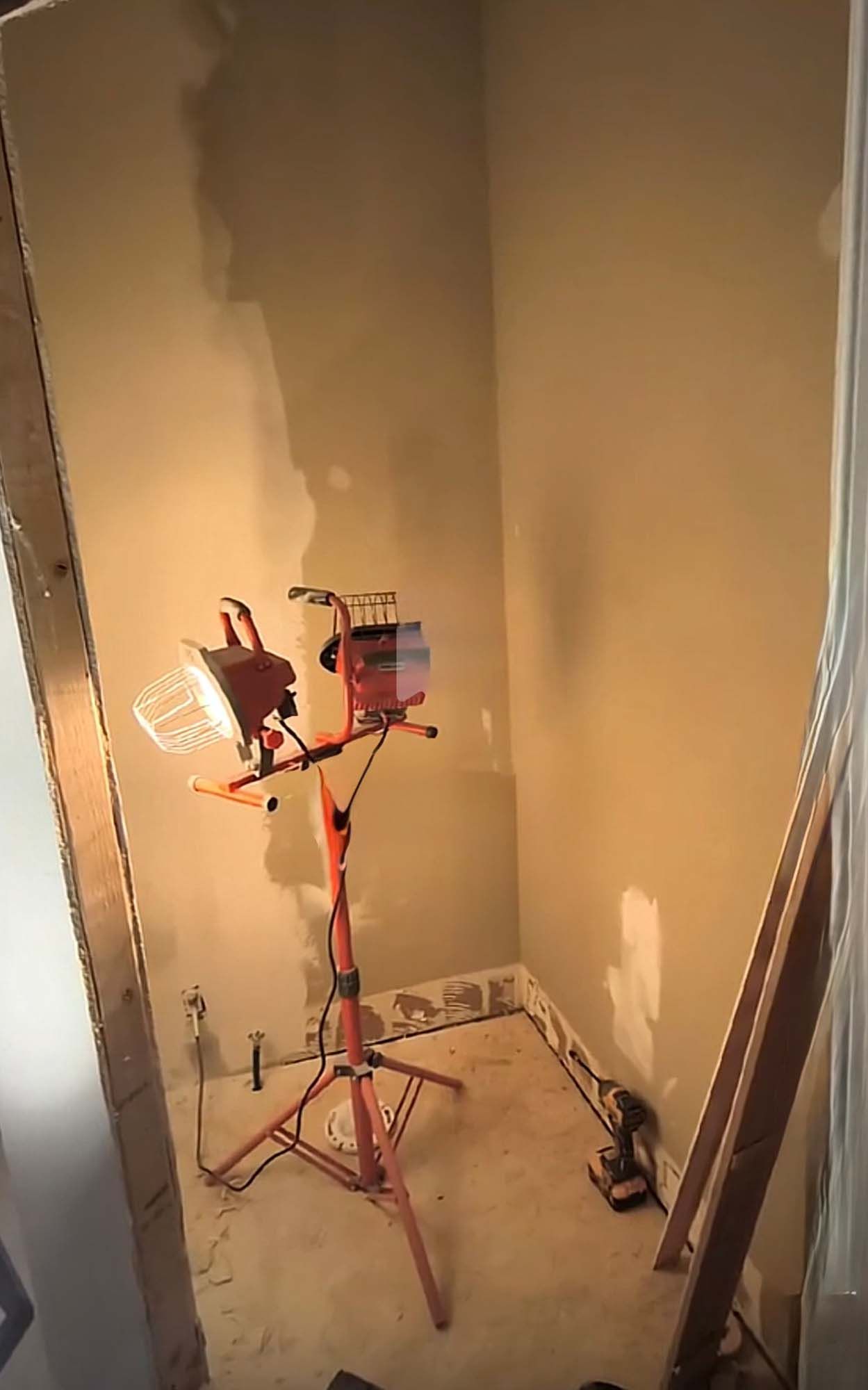 An orange work light illuminates a small room under construction; bare walls and floor.