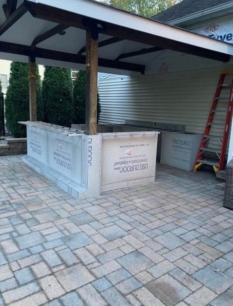 Outdoor kitchen under construction; bar with stone pavers, wooden beams and posts.
