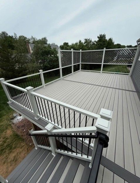 Gray composite deck with black railings and lattice fencing, overlooking a yard under a cloudy sky.