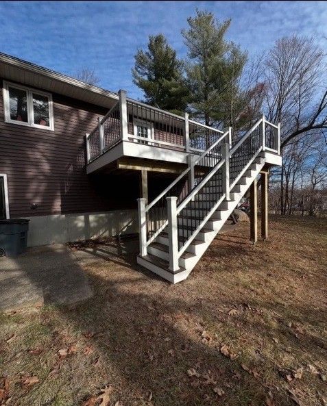 Deck with white and black railings, attached to a brown house with outdoor stairs leading to the yard.