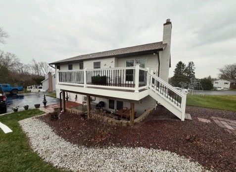 White-sided house with a white deck and black railings. Brown landscaping surrounds. Overcast day.
