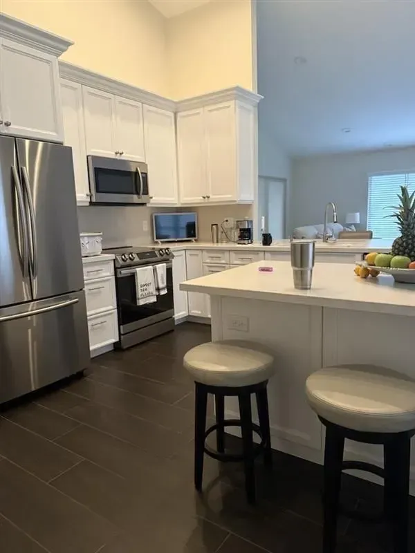 Kitchen with white cabinets, stainless steel appliances, dark wood floor, and island with stools.