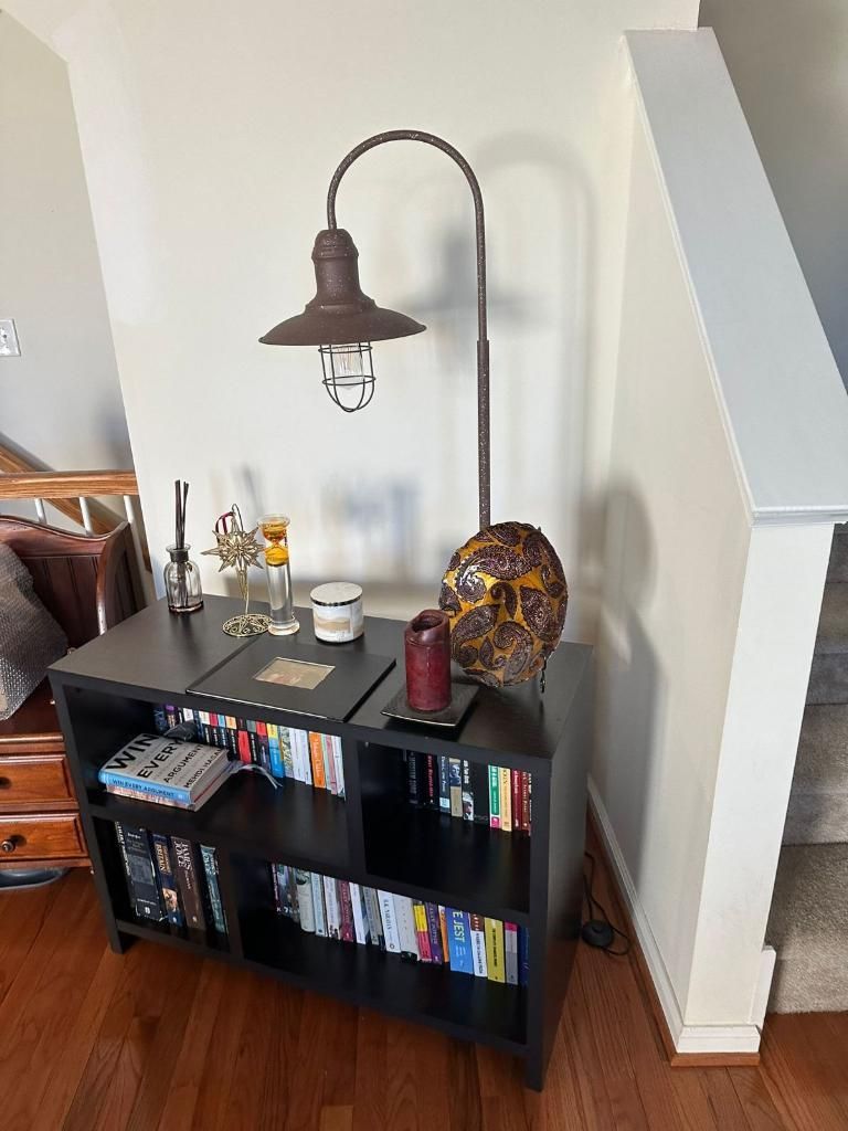 Black bookshelf with lamp, skull, candles, and books, next to stairs.