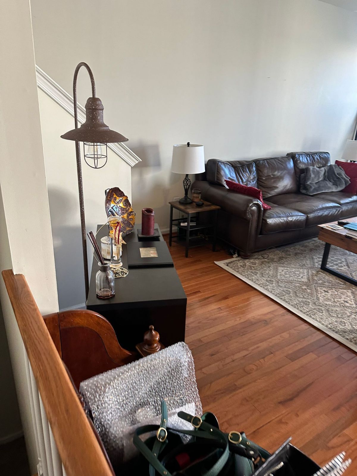 A living room with a brown leather couch, wooden floor, lamp, and dark console table.