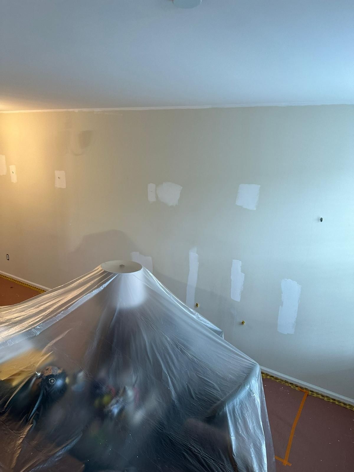 Interior room being painted, wall patches visible, furniture covered with plastic sheeting.