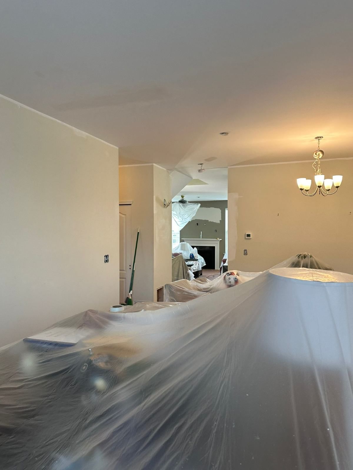 Interior room being painted, furniture covered in plastic, walls and ceiling are white.
