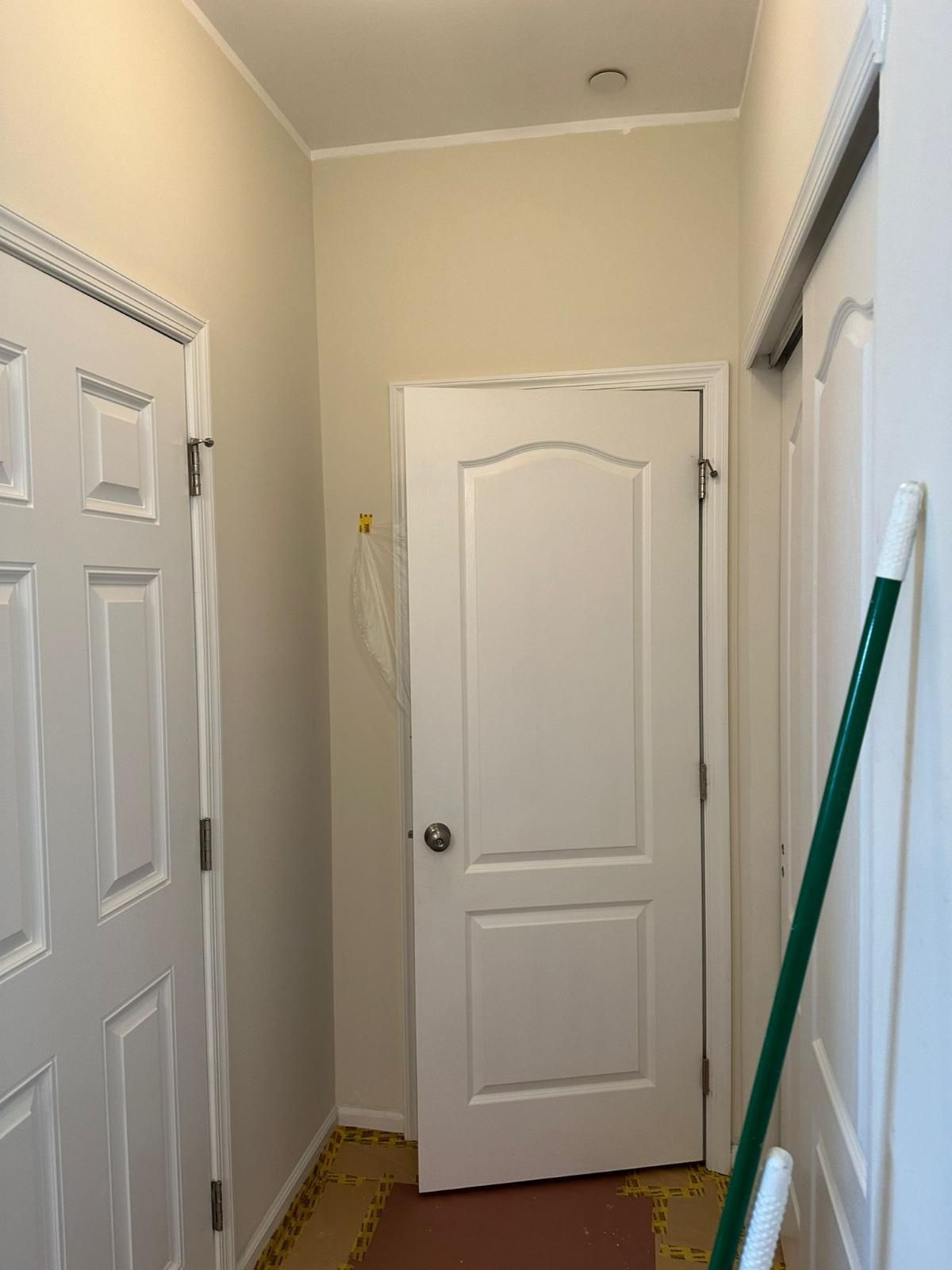 Hallway with white doors and beige walls; a green broom leans against a closet door.
