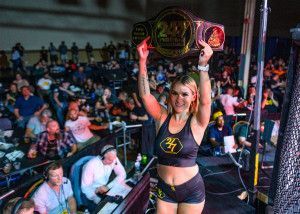 A woman is holding a championship belt in front of a crowd.