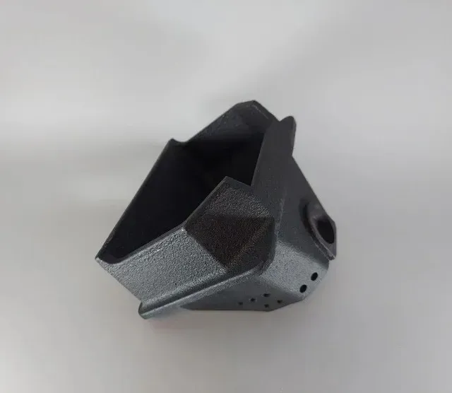 Black 3D-printed mechanical part with angular top and a circular side opening on a gray background