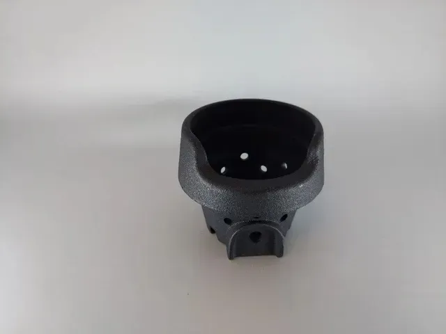 Black plastic cup-shaped device with a small opening and two holes, shown on a light gray surface