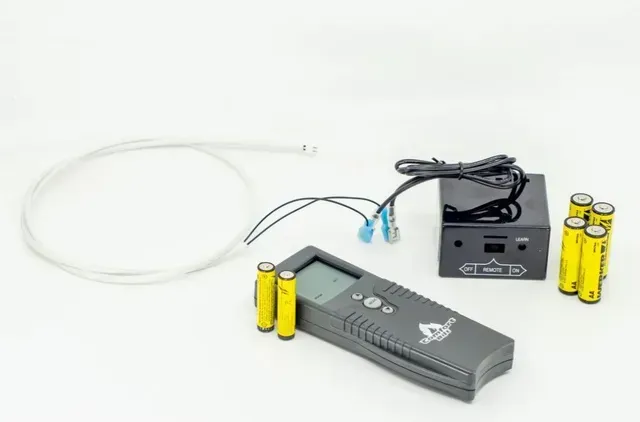 Gray handheld electronic device with cables, sensor, and two yellow batteries on a white background