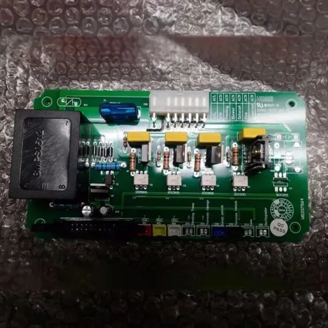 Green circuit board with black transformer, blue capacitor, and white connector on bubble wrap